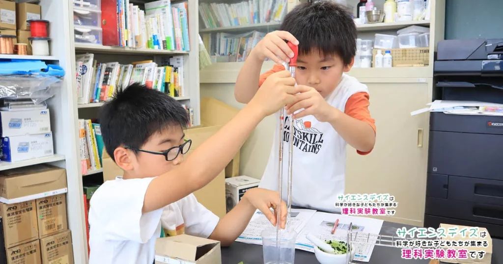 メスピペットでアルコールを準備する小学生低学年の男の子2人 - 実験器具の正しい使い方を身につけるサイエンスデイズの授業風景