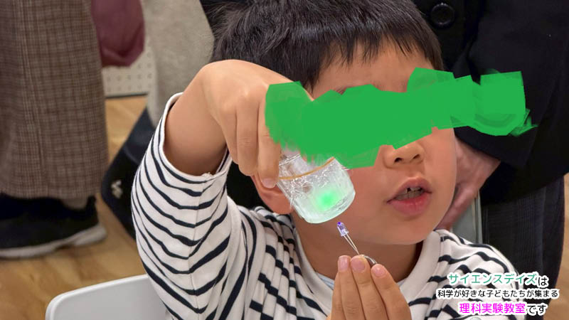 ブラックライトでスライムが緑色に光る様子を驚きの表情で見つめる男の子 - 遊びながら科学の不思議を学ぶサイエンスデイズの体験型イベント