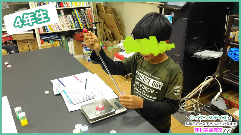 色水の重さをはかりで量り直して比較する小学生 - サイエンスデイズの密度実験