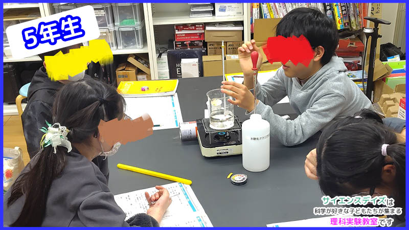 ガスコンロで水を温めてみかんの薄皮除去の準備をする子ども - サイエンスデイズの理科実験教室