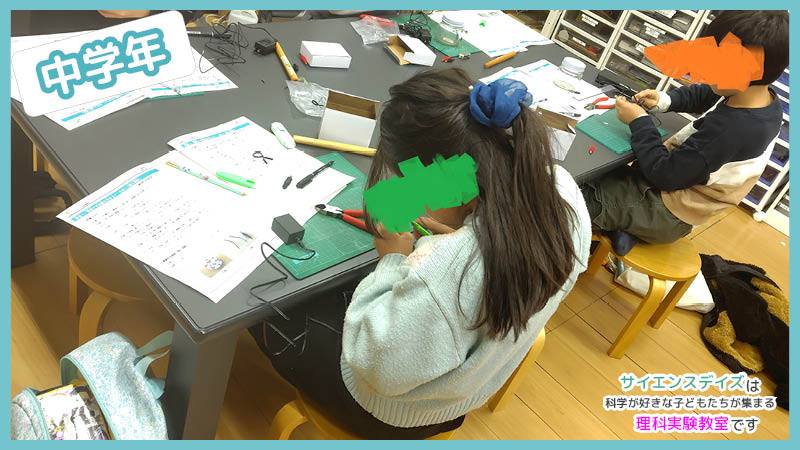 手順書を見ながらみのむしクリップで芯を固定しようとする中学年の子どもたち - サイエンスデイズの理科実験教室