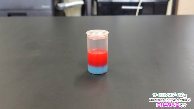30mLのプラスチックバイアルで上の赤い油と下の青い水が分かれている様子